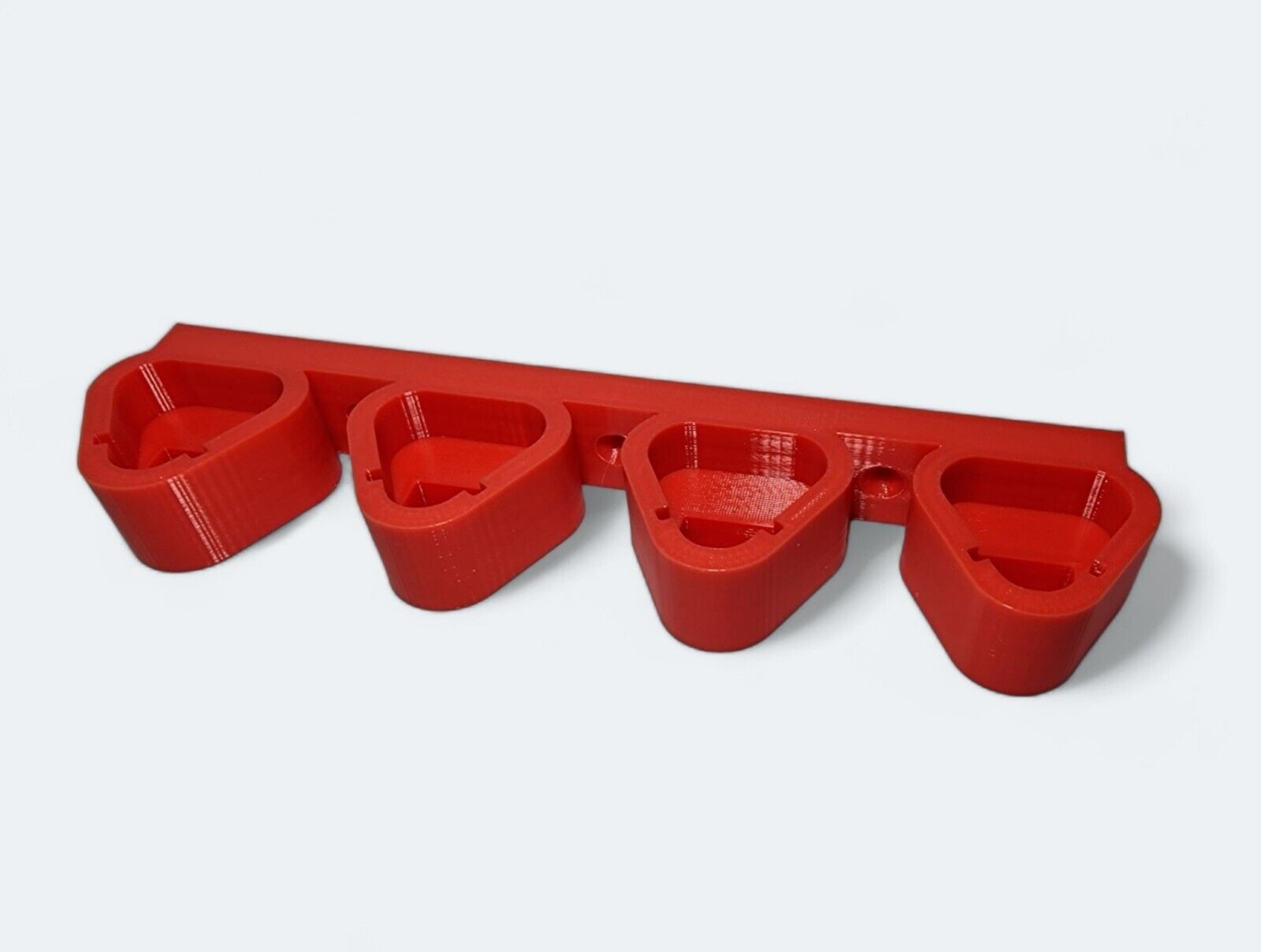 A 3D-printed wall mount in red, featuring four teardrop-shaped holders designed for organizing items such as Milwaukee M12 12V power tool batteries or utensils. The mount's flat back ensures easy and secure attachment to a wall.