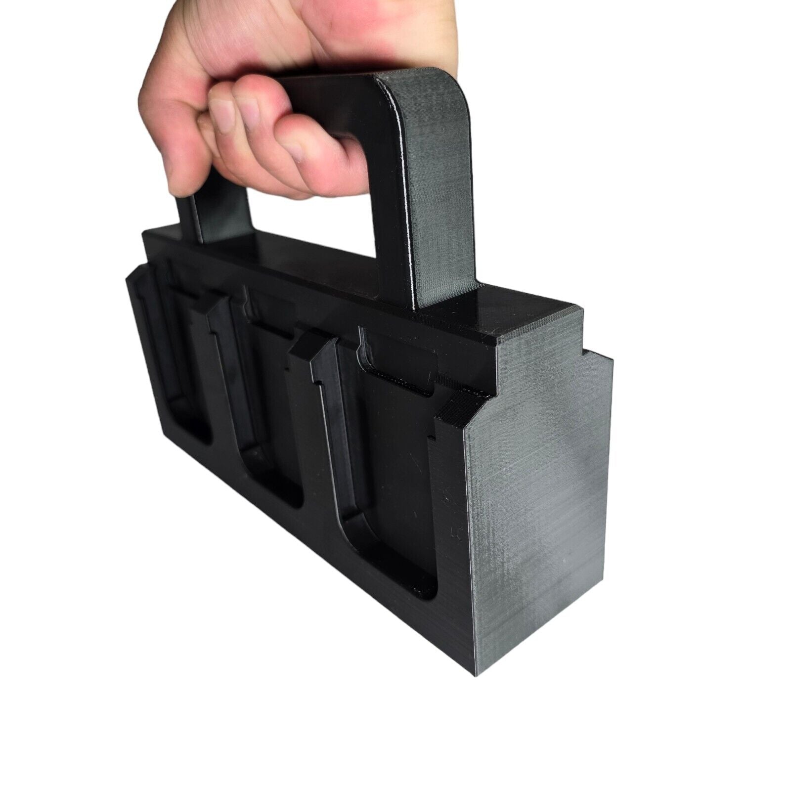 A person is holding a black, rectangular plastic HEAVY DUTY 6X Battery Basket Carrier Caddy Holder for Makita, featuring three block-shaped components, and resembling a 3D-printed handheld tool or device, against a plain white background.