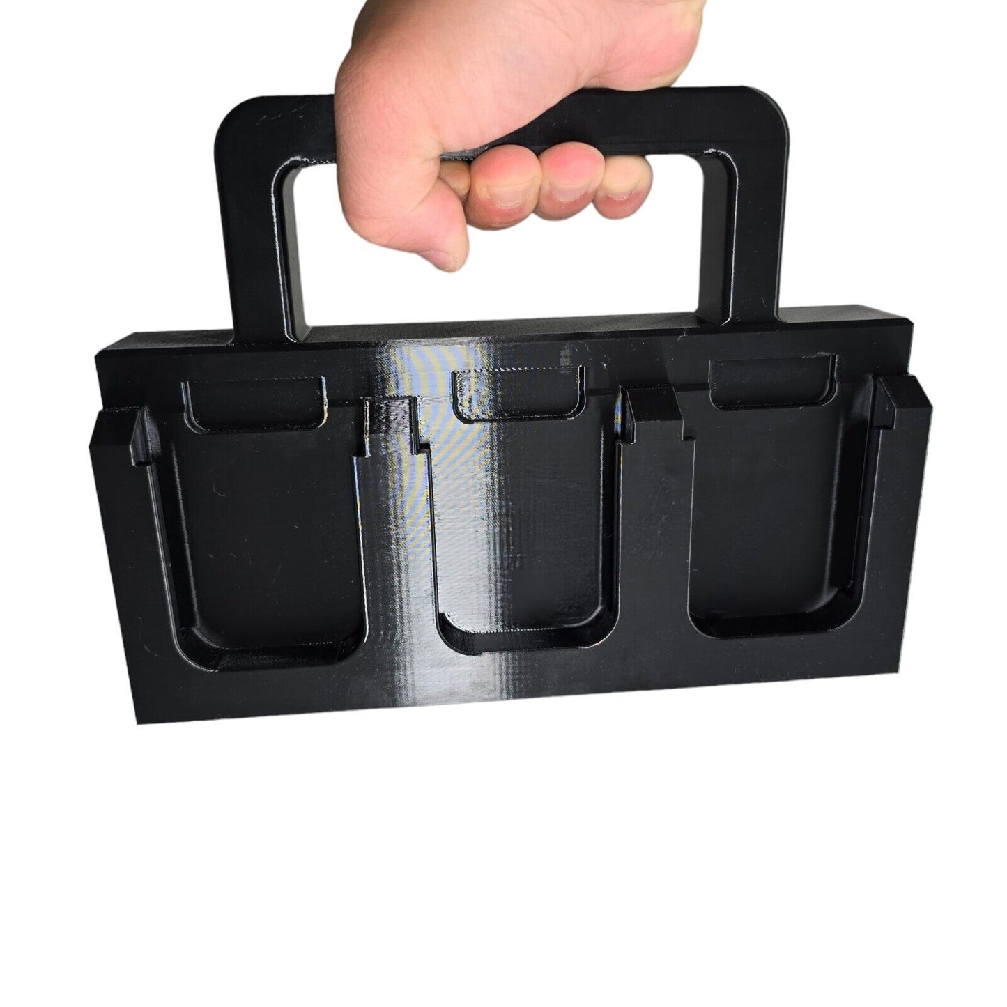 A hand holds a 3D printed, black plastic HEAVY DUTY 6X Battery Basket Carrier Caddy Holder for Makita, featuring three compartments and a sturdy handle for easy carrying. The background is white.