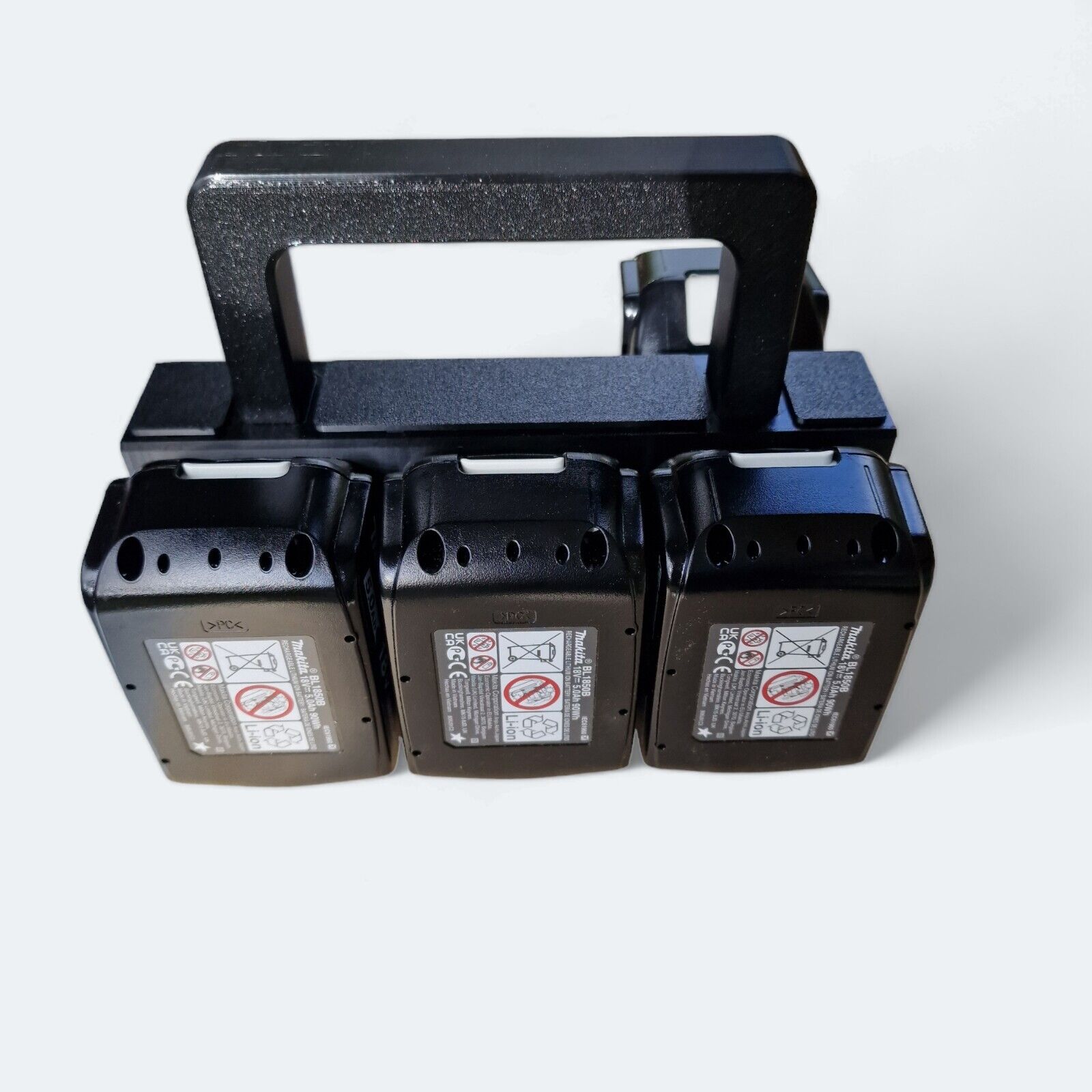 The 6x Battery Basket Carrier Caddy Holder for Makita, in an elegant black design, efficiently arranges three 18V Makita batteries, each featuring warning icons. Constructed from durable plastic and equipped with a convenient handle, this Battery brand carrier ensures easy portability.