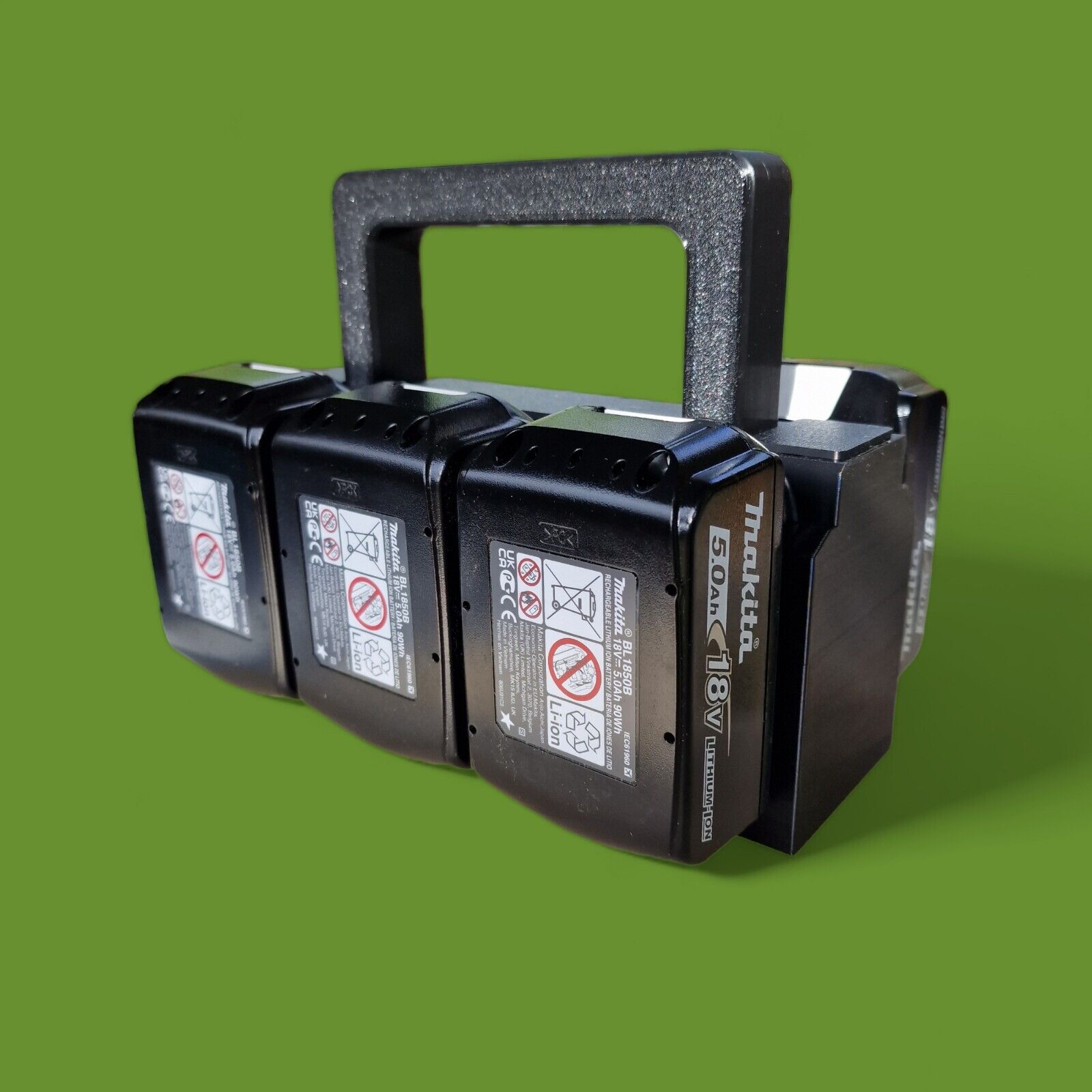 A Battery 6x Carrier Caddy Holder for Makita with three storage compartments, featuring three black 18V lithium-ion batteries arranged together on a green background. The caddy includes a carrying handle along with various safety and product labels on each battery.